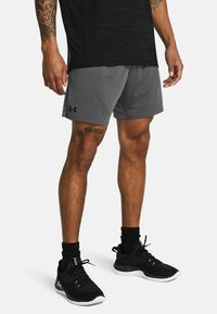 Graue Sportshorts mit einem elastischen Bund und seitlichen Taschen, kombiniert mit schwarzen Schuhen mit weißen Sohlen und schwarzen Socken.