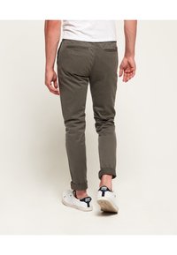 Chino khaki dal taglio slim, con cuciture visibili, due tasche posteriori e orli arrotolati. Abbinati a sneakers bianche.