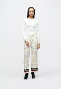 Valge soonikkoes pika varrukaga topp, mis on sobitatud laia lõike ja kuldsete ning hõbedaste kettmustritega pükstega. Mustad kontsaga pahkluu saapad.