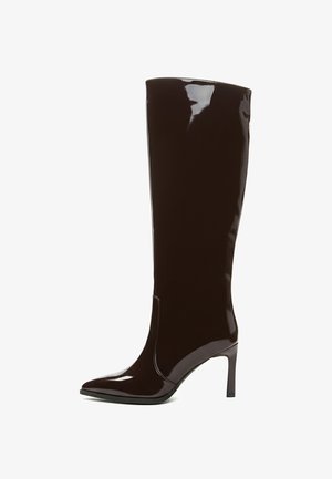 Bottes brunes à talons hauts et mi-mollet, fabriquées en matériau verni brillant, avec un bout pointu et un design épuré avec des coutures minimales.