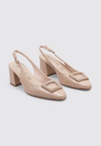 Zapatos de tacón bajo en color beige con tirante trasero, con un acento cuadrado en la puntera, textura de cuero suave y una correa ajustable en el tobillo.