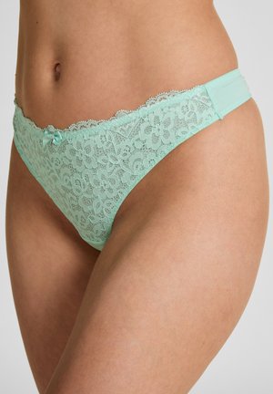 Frau trägt mintgrüne, blumige Spitzen-Bikini-Unterwäsche mit einer kleinen Schleife vorne an der Taille.