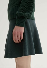 Suéter de punto verde oscuro con costuras texturizadas y mangas acampanadas, combinado con una falda acampanada, también en verde oscuro, hecha de una tela suave.
