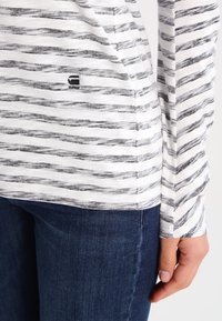 Langarmhemd mit horizontalen schwarz-weißen Streifen, aus leichtem Stoff, mit einem kleinen "RAW"-Logo nahe dem Saum.