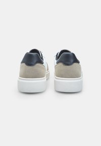 Valged tennisjalatsid halli seemisnahaga ja tumesiniste aktsentidega. Paksem kummist sisetald, tekstureeritud serv ja kontrastsete materjalikihtidega kand.