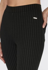 Zwart gestreepte leggings met een zachte textuur, voorzien van dunne witte streepjes en een klein zilveren logo op de tailleband.