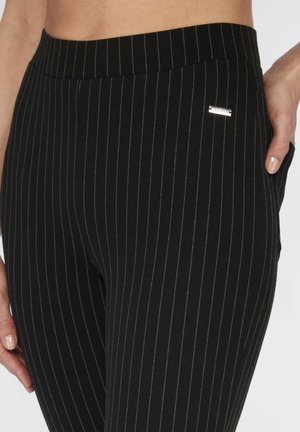 Zwart gestreepte leggings met een zachte textuur, voorzien van dunne witte streepjes en een klein zilveren logo op de tailleband.