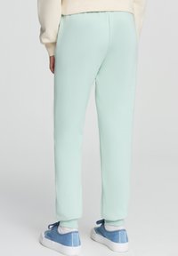 Jasno miętowe spodenki dresowe o zwężanym kroju, miękka faktura, elastyczny pas i ściągacze na końcach nogawek. Połączone z niebieskimi trampkami.