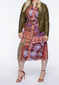 Multicolored patchwork dress with floral and geometric patterns, cinched waist, and a lightweight texture, paired with a brown leather jacket.