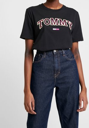 Czarna bawełniana koszulka z logo "TOMMY" w kolorze czerwonym i białym, noszona z wysokim stanem ciemnoniebieskich dżinsów. Krótkie rękawy i okrągły dekolt.