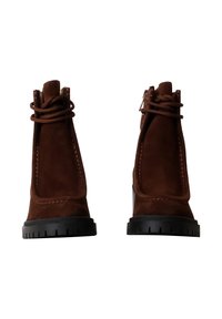 Botas de tobillo de ante marrón con punta redondeada, cordones anudados y suela de goma negra texturizada. Presenta acentos de costura en contraste.