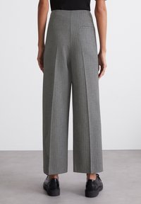 Graue weite Hosen mit vertikalen Streifen, hohem Bund, einer einzelnen Gesäßtasche und einer glatten Stoffbeschaffenheit. Kombiniert mit schwarzen Schuhen.