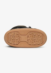 Zapato negro con una suela de goma texturizada que presenta patrones redondeados y ranuras, destacando la adherencia y la flexibilidad. Parte inferior de color natural.