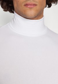 Suéter blanco de cuello alto hecho de una tela suave y elástica. Presenta un diseño ajustado con un cuello alto y una textura suave.