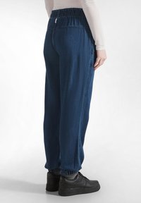 Joggers de denim en azul oscuro con cintura elástica y tobillos recolectados. Combinados con zapatillas negras, mostrando un ajuste relajado.
