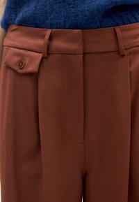 Pantaloni marroni su misura con frontale piatto, dotati di una tasca laterale con bottone e una texture di tessuto liscia e morbida.