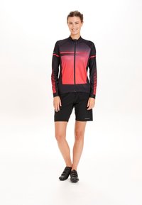 Idrottskläder med en svart och röd gradient zip-up jacka med geometriska mönster, i kombination med svarta shorts och cykelskor.