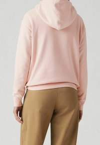 Felpa rosa realizzata in morbido cotone, con cappuccio regolabile, polsini a costine e vestibilità rilassata. Abbinata a pantaloni beige.
