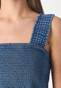 Top azul con frunce, que presenta tirantes anchos de canalé, tejido texturizado y un escote cuadrado. Vista en detalle que resalta la intrincada elaboración.