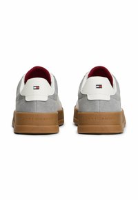 Sneaker in suede grigio con dettagli in pelle bianca e suola in gomma marrone. Presenta un piccolo logo sul tallone e un interno imbottito rosso.