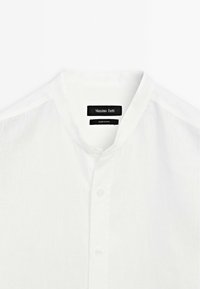White collared shirt with a button-down front, made from lightweight fabric. Features a subtle texture and a label reading "Massimo Dutti."
