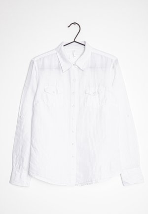 Camisa blanca de manga larga con botones y cuello, que presenta una textura a rayas, dos bolsillos en el pecho y botones blancos en una percha negra.