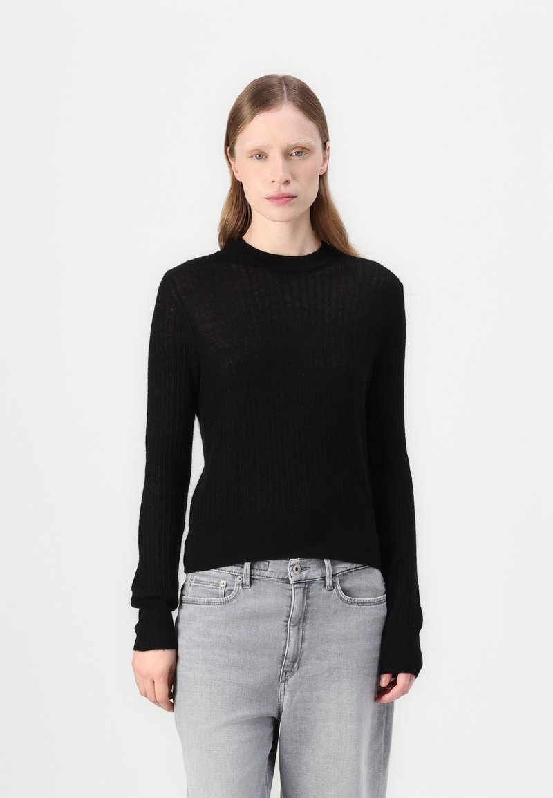Svart ribbet strikkegenser med lange ermer, rund hals og en tettsittende silhuett, kombinert med lysegrå jeans.