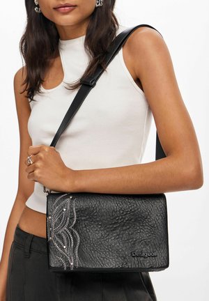 Borsa nera in pelle strutturata, con trattamento texturizzato, dettagli di cucitura bianca intricata e marchio. Include una tracolla removibile e ha una forma rettangolare rigorosa.