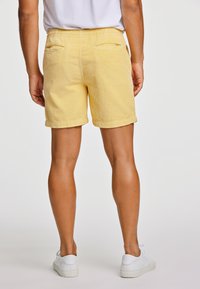 Gula kordflossbyxor med uppvikta fållar, elastisk midja och två bakfickor, kombinerat med vita sneakers på en neutral bakgrund.