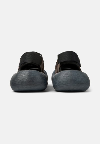 Paire de sandales noires avec semelles épaisses texturées et brides arrière réglables, vues du talon sur un fond blanc.