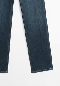 Donkerblauwe spijkerbroekspijpen met een rechte snit en zichtbare stiksels op een witte achtergrond.