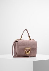 Pieni suorakulmainen käsilaukku pehmeästä vaaleanpunaisesta mokasta, jossa on läppä sulkemiseen. Varustettu kultaisilla yksityiskohdilla, yläkahvalla ja irrotettavalla olkahihnalla.