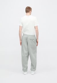 Svetlo sive trenirka hlače z elastičnim pasom in žepom zadaj, kombinirane z belo majico brez potiska. Mehka tkanina, sproščen kroj.