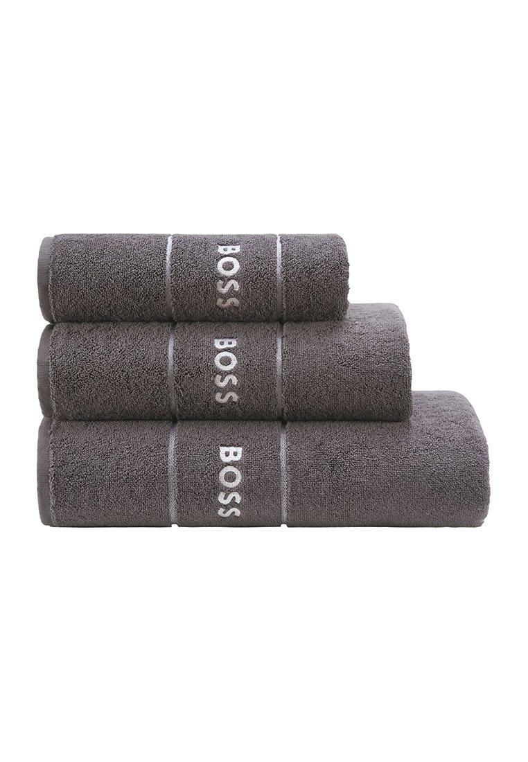 Tre staplade handdukar i mörkgrå färg, tillverkade av plyschfrotté. Varje handduk har vit broderad "BOSS"-logotyp och horisontella ränder.