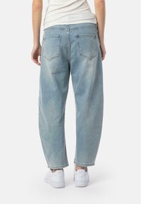 Jean taille haute bleu clair à coupe loose, avec deux poches arrière et un ourlet retroussé, associé à des baskets blanches.