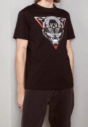 Czarna bawełniana koszulka z grafiką syczącego pantery w szaro-żółtych kolorach w czerwonym trójkącie. Krótkie rękawy i okrągły dekolt.