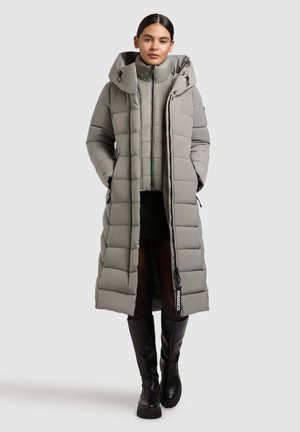 Long puffer coat in light gray, featuring a wide hood, quilted pattern, and zip closure. Paired with a cropped inner jacket and tall black boots.