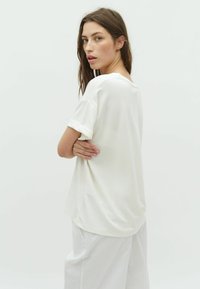 Camiseta de algodón blanca de manga corta con cuello redondo, corte relajado y puños enrollados, combinada con pantalones de pierna ancha de color claro.