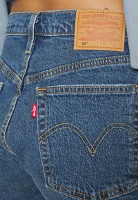 Mörkblå denimjeans med en läderbakpatch som har "Levi Strauss & Co." och karakteristisk gul sömnad på fickorna.
