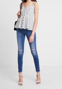 Bílo-černý pruhovaný peplum top s knoflíkovou přední částí, spárovaný s obnošenými modrými skinny džíny a bílými lodičkami na kotníku.