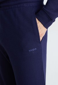 Navyblaue Jogginghosen aus strukturiertem Stoff mit einer Seitentasche und einem sichtbaren "HUGO"-Logo aus hellblauem Garn.