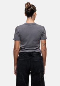 T-shirt grigio a maniche corte, in morbido cotone, con una forma aderente. Jeans neri a vita alta e gamba larga, dotati di tasche e in tessuto testurizzato.