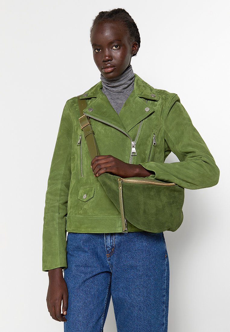 Grüne Wildleder-Motorradjacke mit Reißverschlusstaschen, schmalem Kragen und strukturiertem Finish, kombiniert mit einer passenden grünen Schultertasche.