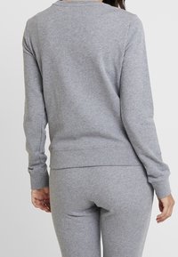 Sudadera gris de manga larga con cuello redondo y puños acanalados. Fabricada en una tela suave, ajustada en la cintura y con una textura lisa.