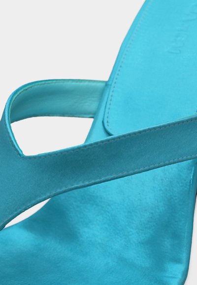 Κοντινό πλάνο ενός σανδαλιού από τιρκουάζ δέρμα που παρουσιάζει λείες λουριά και λεπτομέρειες ραφής στο πέλμα και το πάνω μέρος.