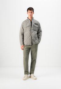 Quilted gray jacket with a stand collar, snap buttons, two chest pockets, and green trousers, paired with cream sneakers.