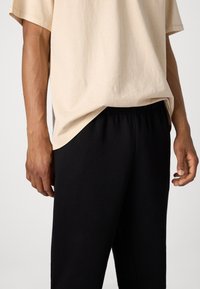 Camiseta de algodón beige con un corte relajado, combinada con pantalones negros de cintura elástica. La camiseta presenta una textura suave y costuras sutiles.