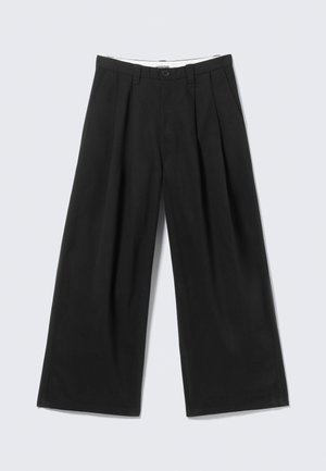 Pantaloni neri a gamba larga con pieghe, passanti per cintura e chiusura con bottone, mostrati su uno sfondo grigio chiaro.