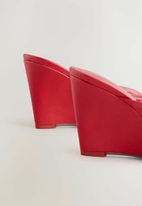 Paari punaseid konksu-tingeid, mille tekstuur on sile, nähtavad tagant neutraalsel heledal taustal.
