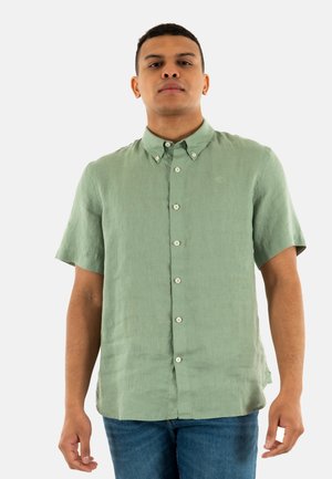 Camicia a maniche corte, con bottoni, in tessuto verde chiaro con una finitura testurizzata, caratterizzata da un colletto classico e bottoni bianchi davanti.